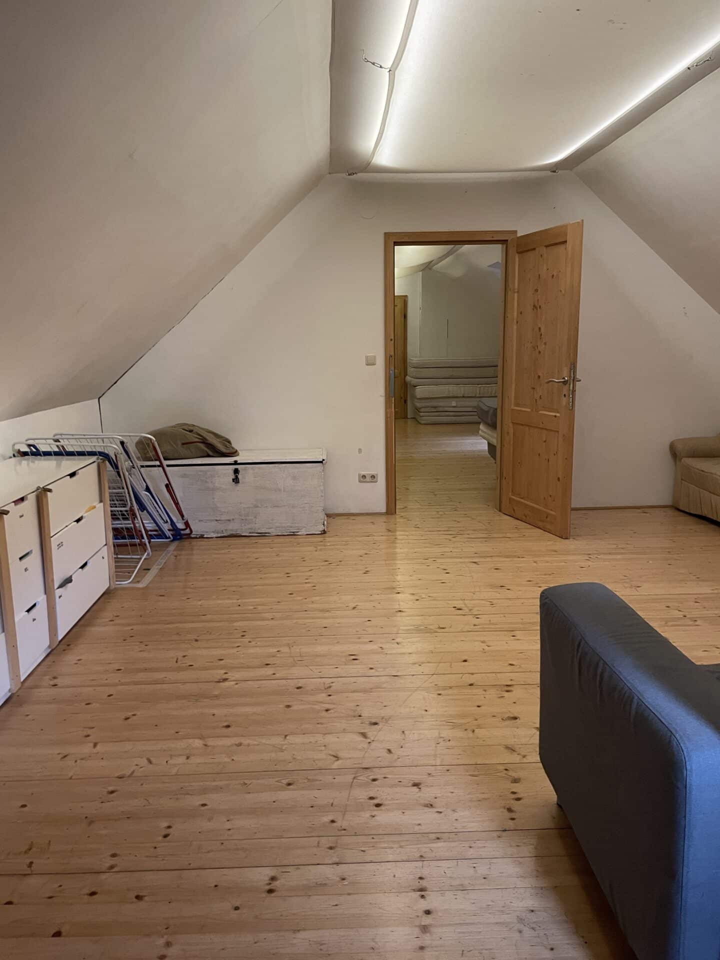 Am Foto ist der Vorraum am Dachboden mit zwei Couches zu sehen. Durch eine Tür sieht man den ersten, großen, Raum mit sehr vielen Matratzen. Im Vorraum ist außerdem ein Kasten und Wäscheständer zu sehen.